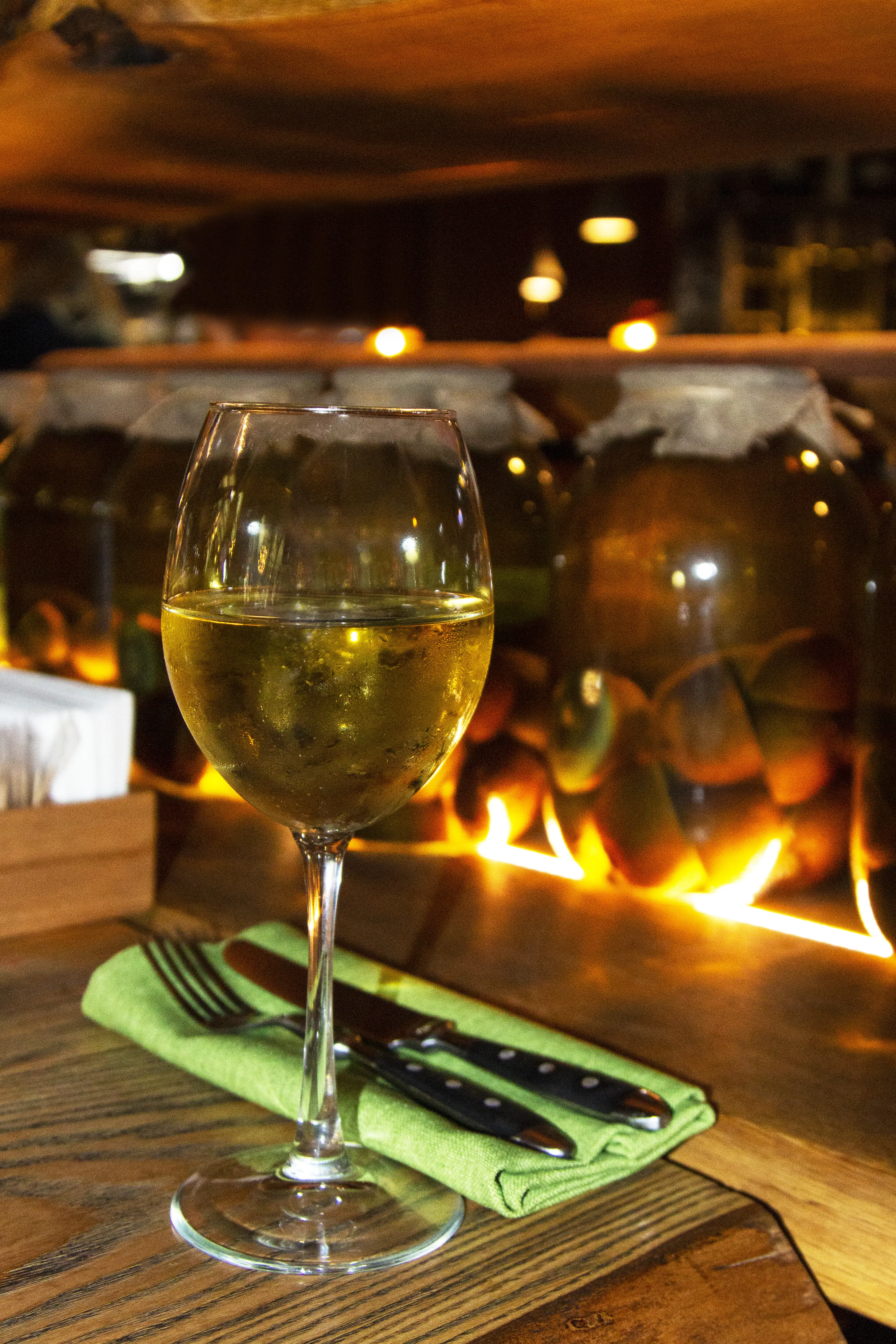 A glass of white wine with a blurry background of canned fruit in a dark bar. One glass of grape wine.