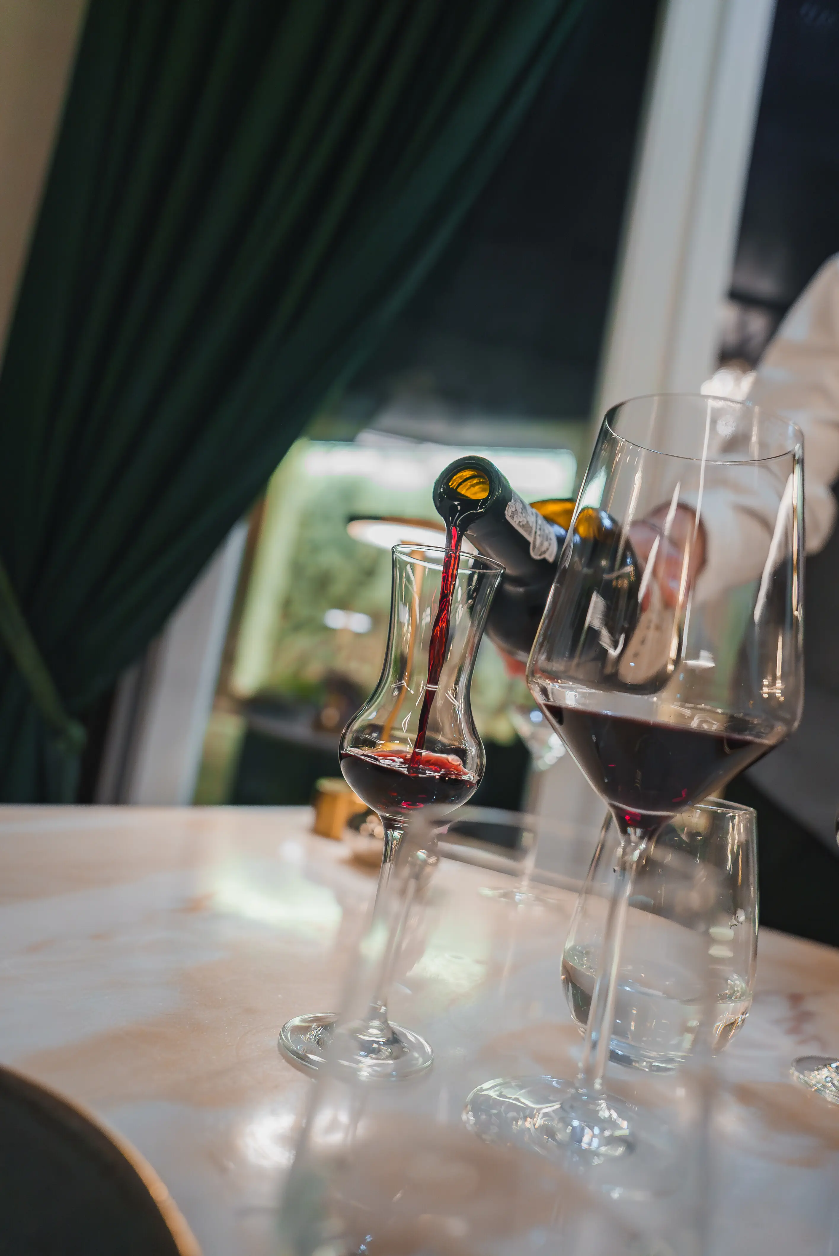 In a luxurious hotel dining room, a sommelier pours red wine into a decanter.